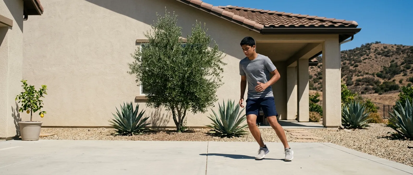 A teenager doing footwork on a sunlit concrete patio behind a stucco house with a tile roof, agave and gravel planting, dry hills rising behind.